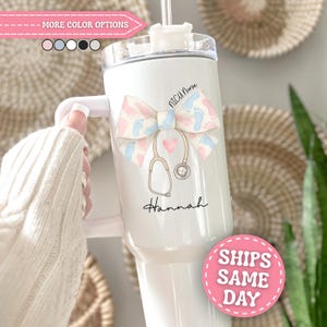 May include: A white stainless steel tumbler with a handle and a clear lid. The design features a large bow with a pink and blue baby footprint pattern, a stethoscope, a small pink heart, and the text NICU Nurse and the name Hannah.
