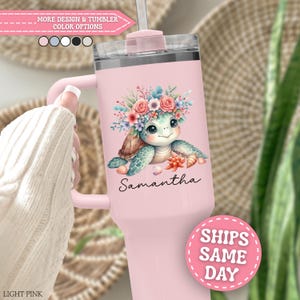 May include: A light pink stainless steel tumbler with a handle and a clear lid. The front features a graphic of a sea turtle wearing a floral crown, surrounded by seashells and a starfish, with the name Samantha printed in black script below.