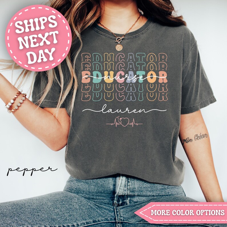 May include: Dark gray t-shirt with the words "Educator Nurse" in colorful, stacked text. The name "Lauren" is written below in cursive, with a nurse symbol and heartbeat graphic. A pink circle with "SHIPS NEXT DAY" is in the upper left.