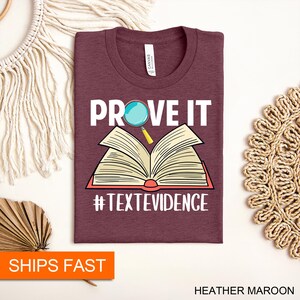 Puede incluir: Una camiseta color marr&oacute;n con el texto "PROVE IT" en letras blancas. Una lupa est&aacute; sobre la palabra "PROVE". Un libro abierto est&aacute; debajo del texto. El texto "#TEXTEVIDENCE" est&aacute; debajo del libro.