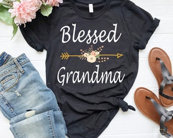 Könnte beinhalten: Schwarzes T-Shirt mit weißem Text "Blessed Grandma" und einem floralen Pfeil-Design.