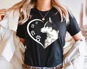 May include: Black t-shirt featuring a white heart with paw prints and a detailed illustration of a husky dog with blue eyes. The dog's fur is black and white. The shirt is a classic crew neck.