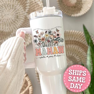 May include: White tumbler with a floral design and the word "MAMAW" in retro font. The tumbler features the names Isabella, James, and Olivia. The text "LOVE THEM, RAISE THEM KIND, WATCH THEM GROW" is printed above the floral design.