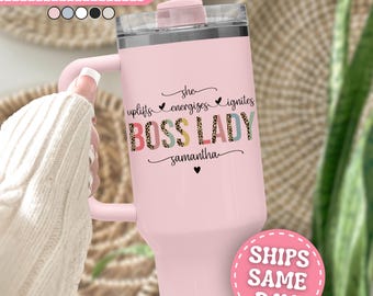 Puede incluir: Un vaso térmico de color rosa claro con asa y tapa transparente que incluye una pajita. El texto dice she uplifts energizes ignites BOSS LADY samantha con un pequeño corazón. Las letras de BOSS LADY tienen un estampado de leopardo.