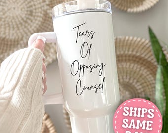 May include: White tumbler with a handle and a clear lid. The tumbler has the text "Tears Of Opposing Counsel" in black script. A pink sticker with the text "SHIPS SAME DAY" is visible.