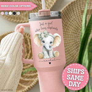 May include: A light pink tumbler with a handle and straw. The tumbler features an illustration of a baby elephant with a floral bow and the text "Just a girl who loves elephants". The name "rachel" is written below the elephant.