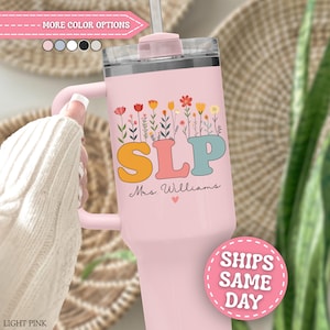 May include: A light pink stainless steel tumbler with a handle and a clear lid. The tumbler features a colorful floral graphic above the letters SLP in a bold font, with the name Mrs. Williams and a small heart printed below the letters.