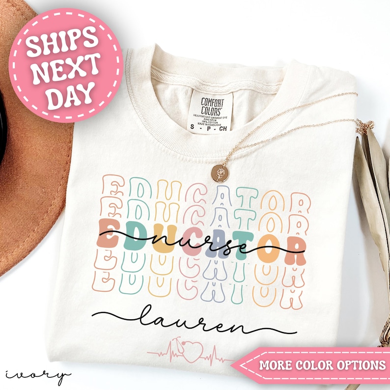 May include: Ivory-colored t-shirt with the word "EDUCATOR" stacked multiple times in pastel colors. The word "nurse" is in a cursive font. The name "Lauren" is written in cursive below. A gold necklace is draped on the shirt.