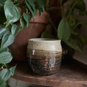 May include: A brown and white ceramic mug with a speckled glaze. The mug has a dark brown band around the middle and a black and brown glaze on the bottom.