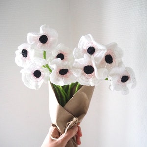 May include: A bouquet of crocheted white flowers with pink centers and black centers. The flowers are wrapped in brown paper and tied with twine.