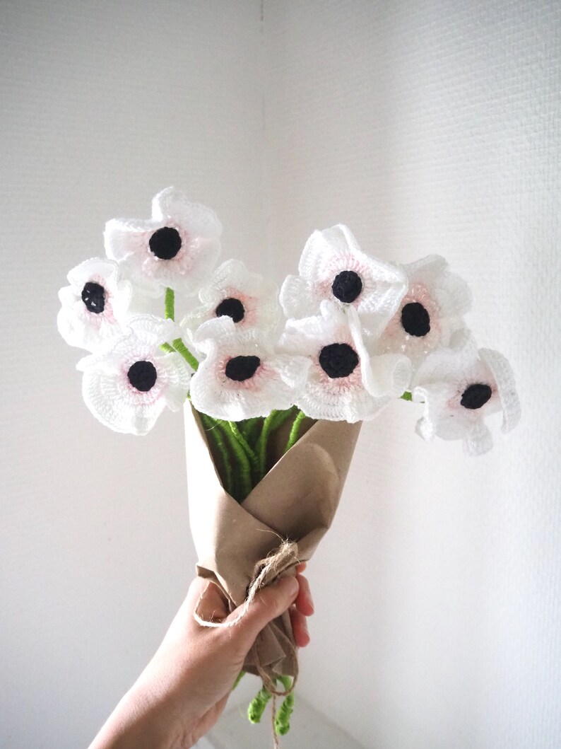 May include: A bouquet of crocheted white flowers with pink centers and black centers. The flowers are wrapped in brown paper and tied with twine.