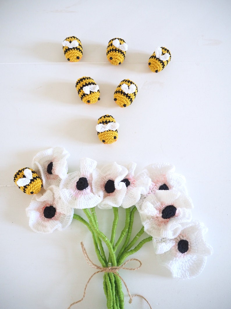May include: A bouquet of white crocheted flowers with pink centers, tied with twine, and surrounded by crocheted bumblebees.