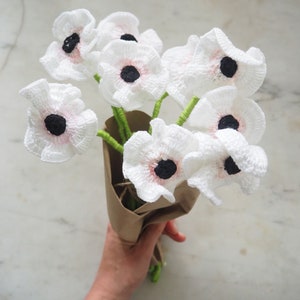 May include: A bouquet of crocheted white flowers with pink centers and black centers. The flowers are wrapped in brown paper.