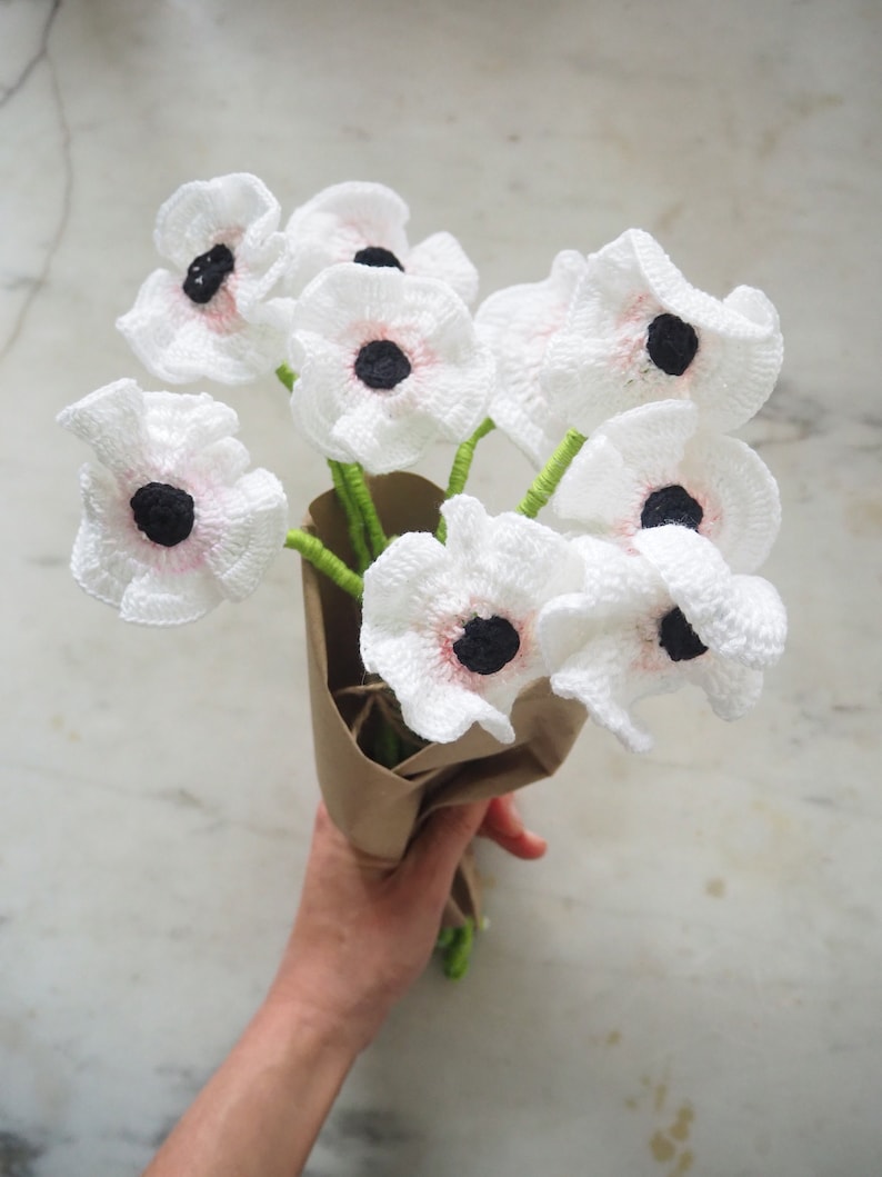 May include: A bouquet of crocheted white flowers with pink centers and black centers. The flowers are wrapped in brown paper.