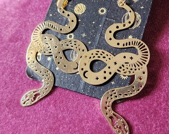May include: A pair of gold snake earrings with a celestial design. The earrings are dangling and have a hook closure.