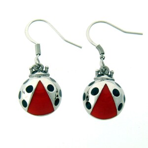 May include: A pair of silver-tone ladybug earrings. Each earring features a silver body with black spots and a red triangle on the lower half. The earrings have a hook closure.