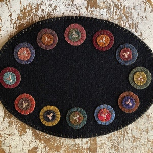 May include: A black felt oval rug with a stitched border and a circle design of colorful felt flowers around the edge.