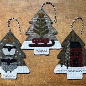 May include: Three felt Christmas tree ornaments with different designs. One features a sheep, another a sled, and the last a small house.
