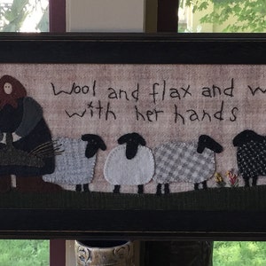 May include: Framed textile art featuring a woman and sheep. The artwork includes the text "She seeketh willingly" and "Wool and flax and worketh with her hands Proverbs 31:13." The sheep are various patterns and colors, set against a neutral background.
