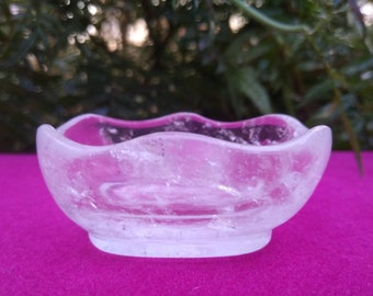 May include: A clear quartz crystal bowl with a wavy edge. The bowl is sitting on a pink surface.