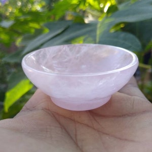 May include: A small, pink, rose quartz bowl. The bowl is smooth and polished, with a slightly translucent appearance.