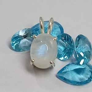May include: A silver pendant with a white moonstone gemstone. The pendant is surrounded by several light blue gemstones.