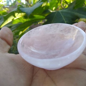 May include: A small, pink rose quartz bowl. The bowl is smooth and polished, with a slightly rounded shape. It is perfect for holding small items, such as crystals or jewelry.