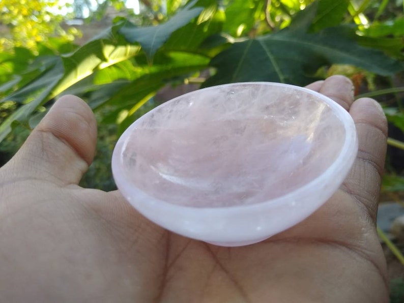 May include: A small, pink rose quartz bowl. The bowl is smooth and polished, with a slightly rounded shape. It is perfect for holding small items, such as crystals or jewelry.