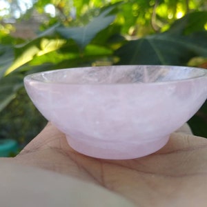 May include: A small, pink, rose quartz bowl. The bowl is smooth and polished, with a slightly iridescent finish.