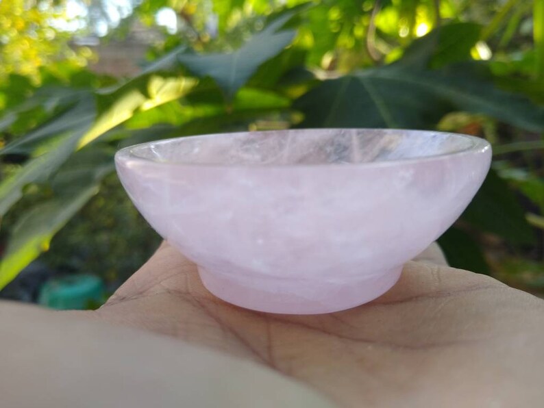 May include: A small, pink, rose quartz bowl. The bowl is smooth and polished, with a slightly iridescent finish.