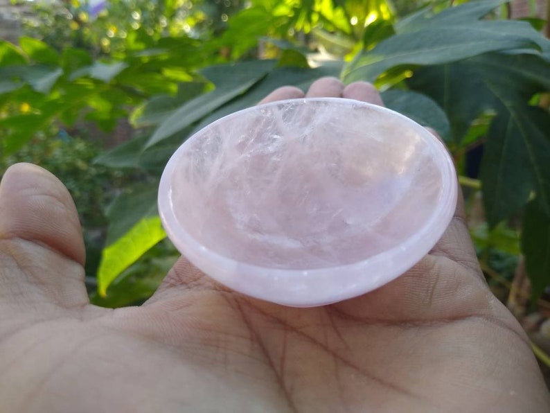 May include: A small, pink, rose quartz bowl. The bowl is smooth and polished, with a slightly rounded shape.