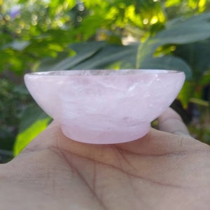 May include: A small, pink, rose quartz bowl. The bowl is smooth and polished, with a slightly rounded shape.