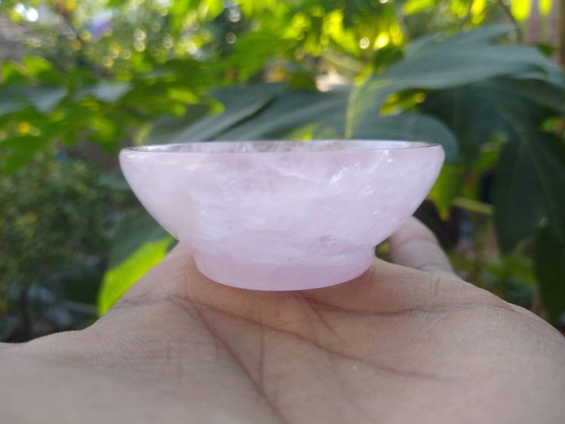 May include: A small, pink, rose quartz bowl. The bowl is smooth and polished, with a slightly rounded shape.