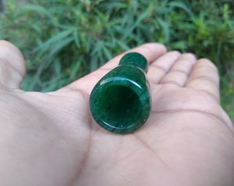 May include: A dark green, smooth, round, polished stone with a hole in the center. The stone is in the palm of a hand.