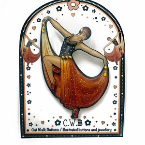 May include: A brown and gold illustrated pin of a woman in a flapper dress dancing. The pin is on a white background with black and gold accents. The text "C.W.B. Cat Walk Buttons / illustrated buttons and jewellery" is at the bottom of the image.