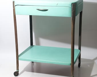 Carrito de servicio vintage de dos niveles con cajón y ruedas, pintado en color turquesa, marca Cosco, mediados de siglo, década de 1960.