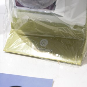 May include: A light green box wrapped in clear plastic. The box has the text "The Widehouse" printed on it. A blue and white card is in the foreground.