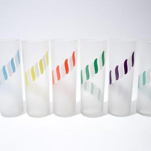 May include: Six frosted glass tumblers with a diagonal stripe design in various colors: blue, yellow, red, green, purple, and teal. The glasses are cylindrical and appear to be empty, set against a white background.