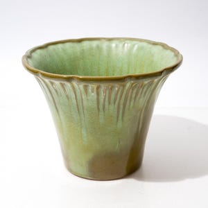 May include: A ceramic planter with a flared, scalloped rim and a glossy finish. The exterior features a gradient of sage green and olive tones, with vertical ribbed detailing that creates a subtle drip effect around the upper portion of the vessel.