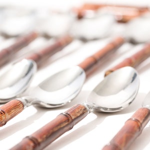 Könnte beinhalten: Ein Satz silberner Löffel mit braunen Bambusgriffen. Die Löffel sind in einer Reihe angeordnet, wobei die Griffe nach rechts zeigen.