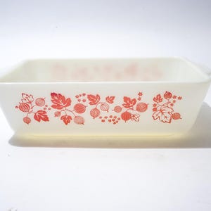 Könnte beinhalten: Rechteckige, cremefarbene Backform mit rotem Blumenmuster. Die Form hat eine leicht ausgestellte Form und kleine Griffe an jedem Ende. Das rote Design zeigt stilisierte Beeren und Blätter.