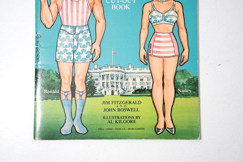 May include: Vintage paper doll book cover featuring illustrations of Ronald and Nancy in patriotic attire. The background shows the White House and a blue sky. The book is titled "Cut-Out Book" and includes the names of the authors and illustrator.