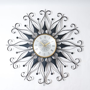 May include: A black metal wall clock with a white face and gold Roman numeral hour markers. The clock has a decorative design with intricate swirls and a black and gold center.