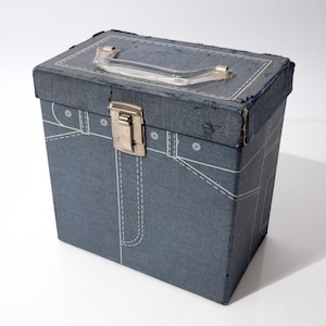 Pode incluir: Uma caixa azul vintage com uma alça de plástico transparente e um fecho de metal. A caixa é decorada com detalhes de costura brancos que se assemelham ao denim. A caixa é retangular e tem uma aparência ligeiramente desgastada.