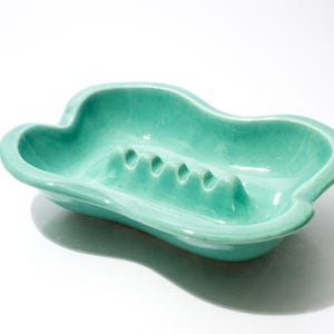 May include: A vintage, turquoise ashtray with a unique, cloud-like shape. The ceramic ashtray features four cigarette rests and a glossy finish. A retro piece for home decor.