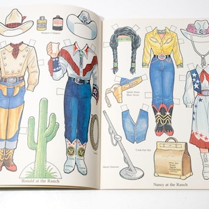 May include: A vintage paper doll book featuring cowboy and cowgirl outfits and accessories. The illustrations include hats, shirts, pants, boots, and a cactus. The text reads "Ronald at the Ranch" and "Nancy at the Ranch".