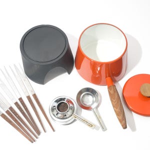 May include: A vintage fondue set with a red pot, black base, and lid with a wooden knob. Includes fondue forks, a burner, and two small ladles. The pot has a wooden handle. The set is designed for serving melted cheese or chocolate.