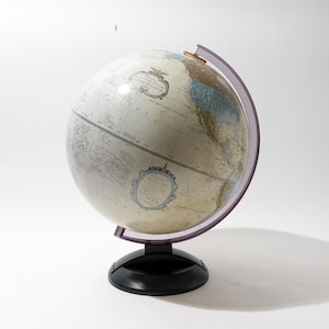 Może przedstawiać: Antyczna kula ziemska z mapą w kolorze kremowym i fioletowym południkiem. Kula stoi na czarnym stojaku.