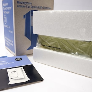 May include: A vintage Westinghouse Sesame Can Opener/Knife Sharpener, packaged in its original box with instruction manuals. The can opener is encased in protective foam and plastic wrap. The box is blue and white.