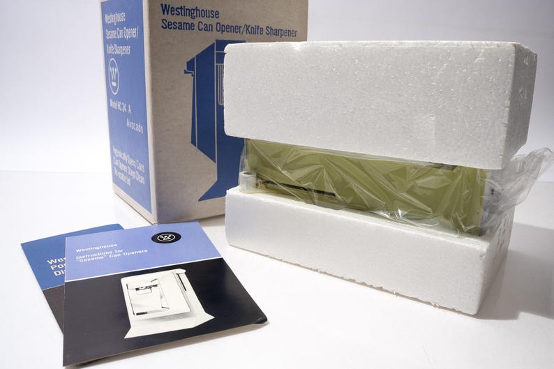 May include: A vintage Westinghouse Sesame Can Opener/Knife Sharpener, packaged in its original box with instruction manuals. The can opener is encased in protective foam and plastic wrap. The box is blue and white.